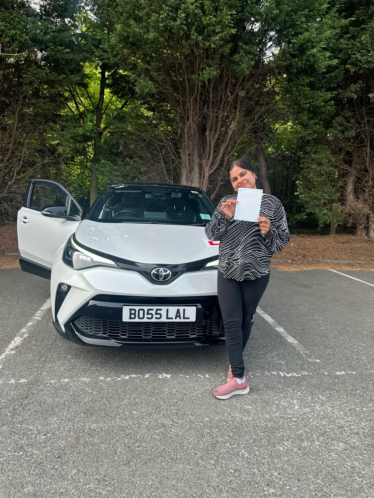 Paramjeet in a patterned top holding a faded pass certificate beside the training car.