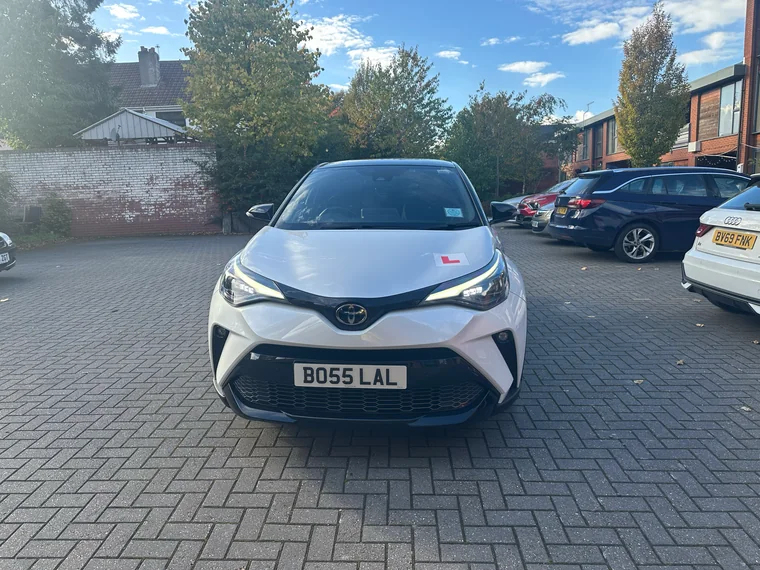 Front view of the white Toyota C-HR GR Sport teaching car with its learner plate.